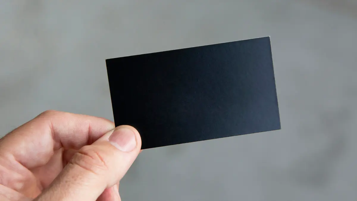 A hand holding up a blank black business card