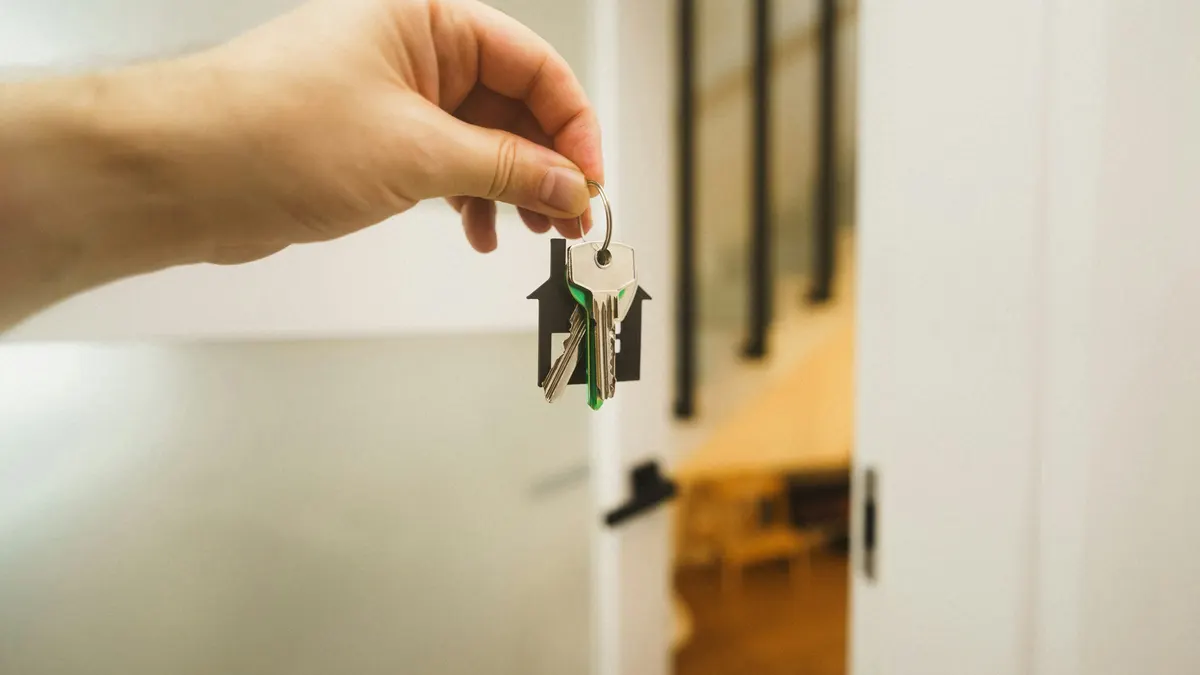 A hand holding a set of house keys on a house-shaped key ring in a doorway