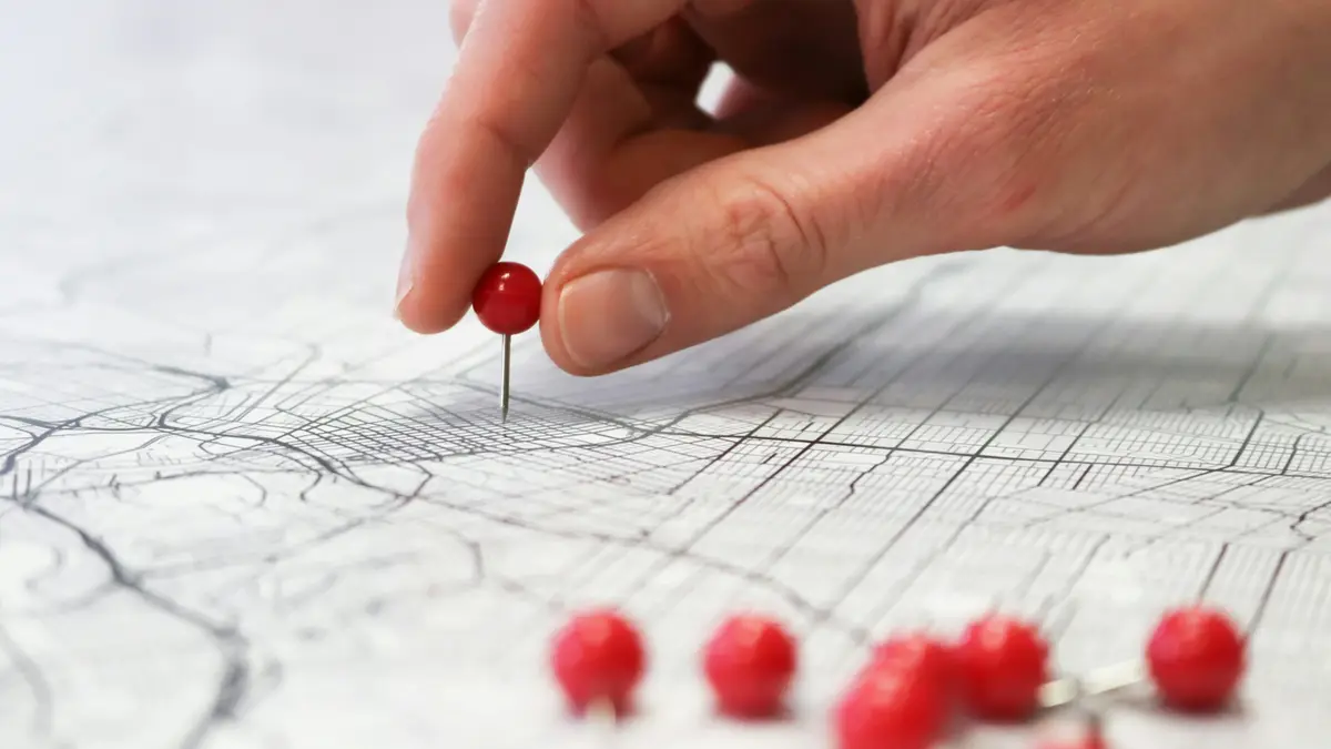 A hand placing a red pin on a street map