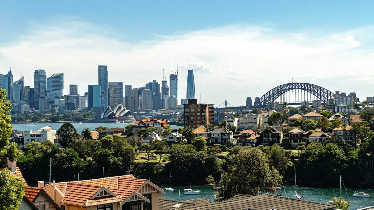 The Sydney skyline and Harbour Bridge seen across the water from a leafy suburb